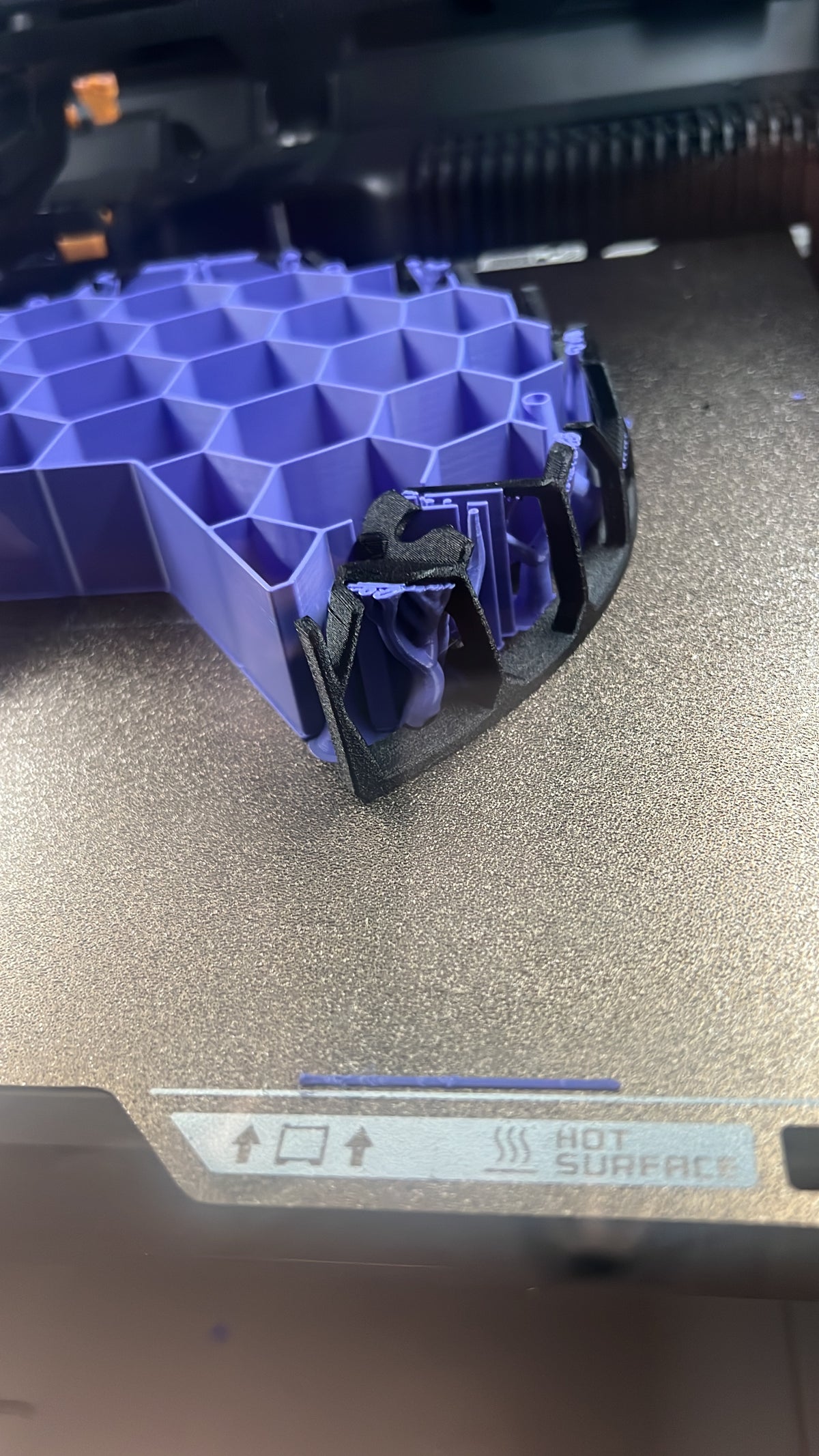 Schwarzer Cage aus TPU-GF während der Fertigung auf dem Druckbett mit violetten Stützstrukturen